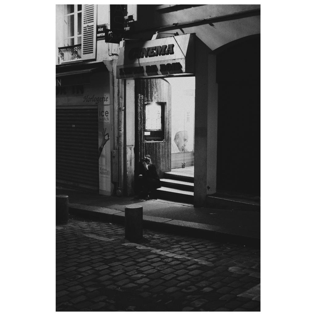photo de rue paris femme assisse dans escalier devanture cinéma noir et blanc
