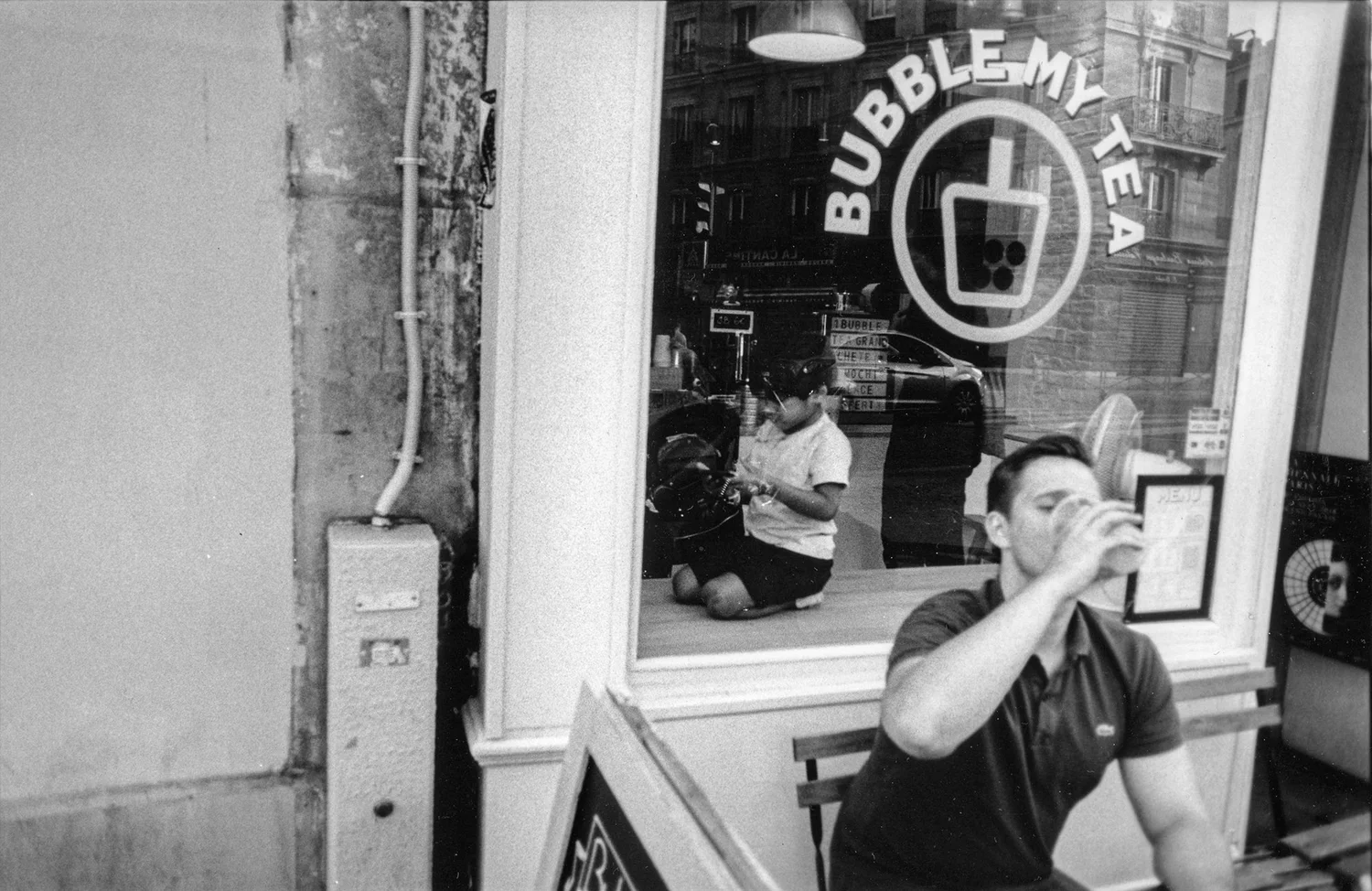street photography homme qui boit sur terrasse avec enfant à l'intérieur dans la vitrine